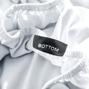 A close-up of a fitted sheet with a label printed with the word 'BOTTOM' in white.