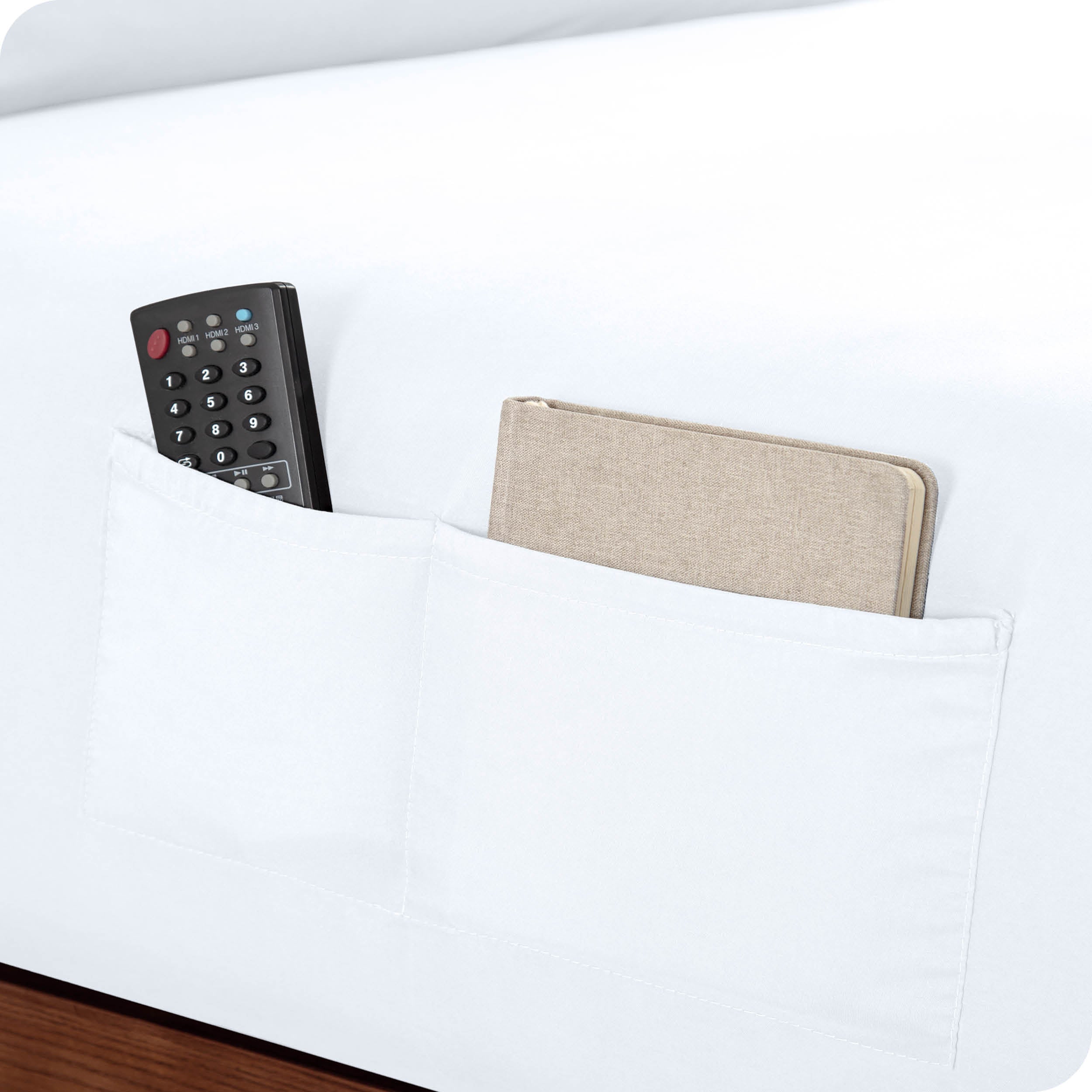 Close up of side pockets on a fitted sheet holding a remote and notebook