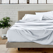 White sheet set on a bed in a room with a white brick wall and plants.