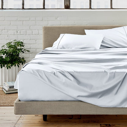 White sheet set on a bed in a room with a white brick wall and plants.