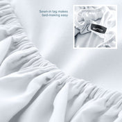 White fitted sheet with a sewn-in tag on a bed, showing close-up of the tag.
