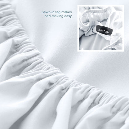 White fitted sheet with a sewn-in tag on a bed, showing close-up of the tag.