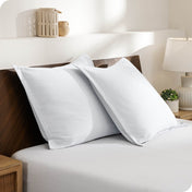 Two pillows with shams on a bed in a bedroom setting with a lamp and decor items.