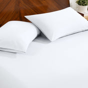 Fitted sheet and pillowcase set on a bed with a dark wood headboard and a small potted plant in the background.