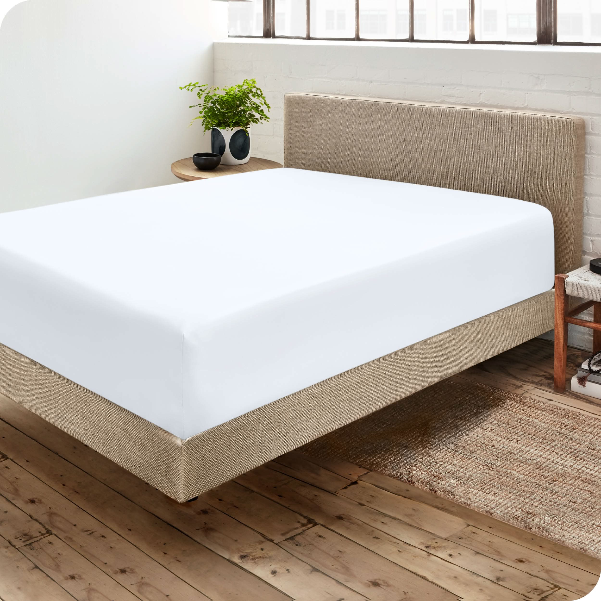 Bedroom with a microfiber fitted sheet on the mattress. A small nightstand is next to the bed with a plant and a bowl on it.