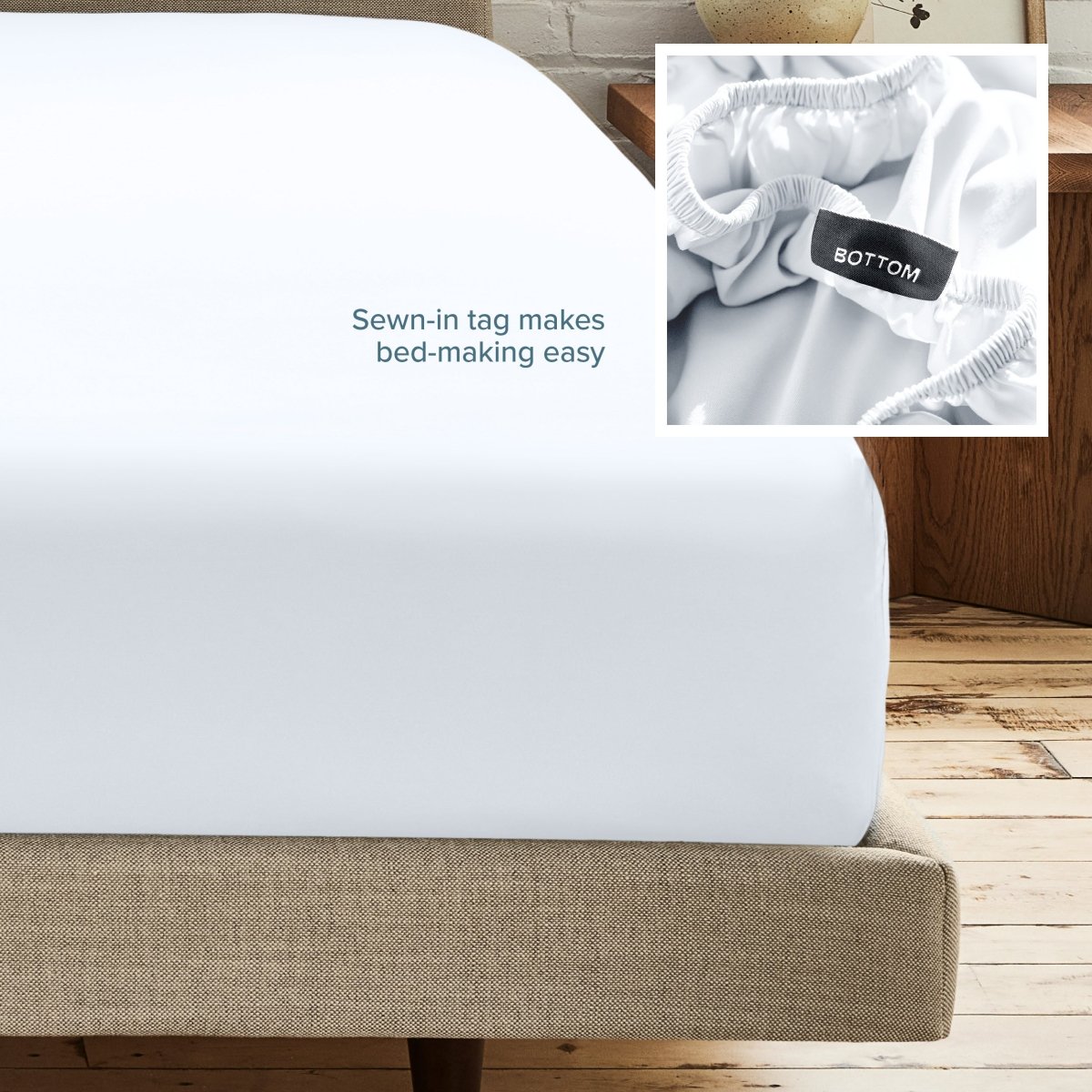 A fitted bed sheet on a bed frame with a small inset close-up of the elastic and a sewn-in tag labeled BOTTOM. White text on the sheet reads, 'Sewn-in tag makes bed-making easy.