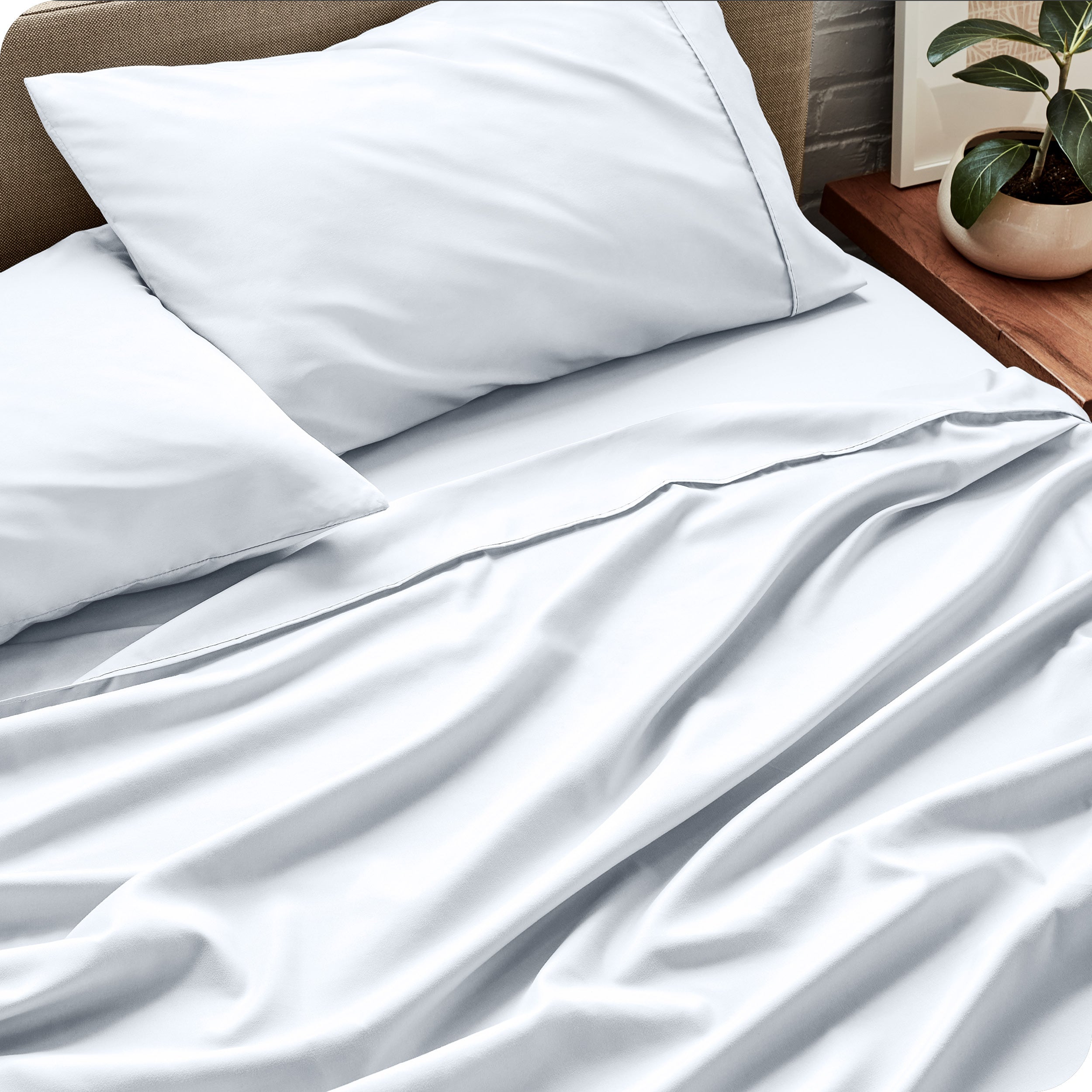Bed sheets and pillows on a bed with a plant in the background