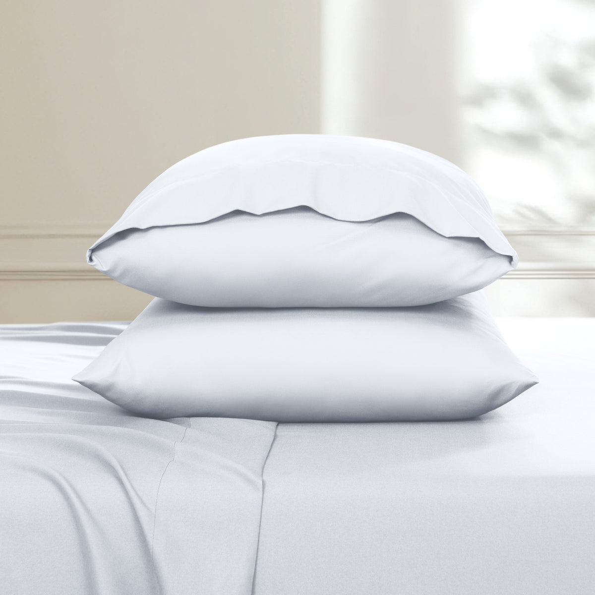 Two pillows stacked on a bed with a neutral background