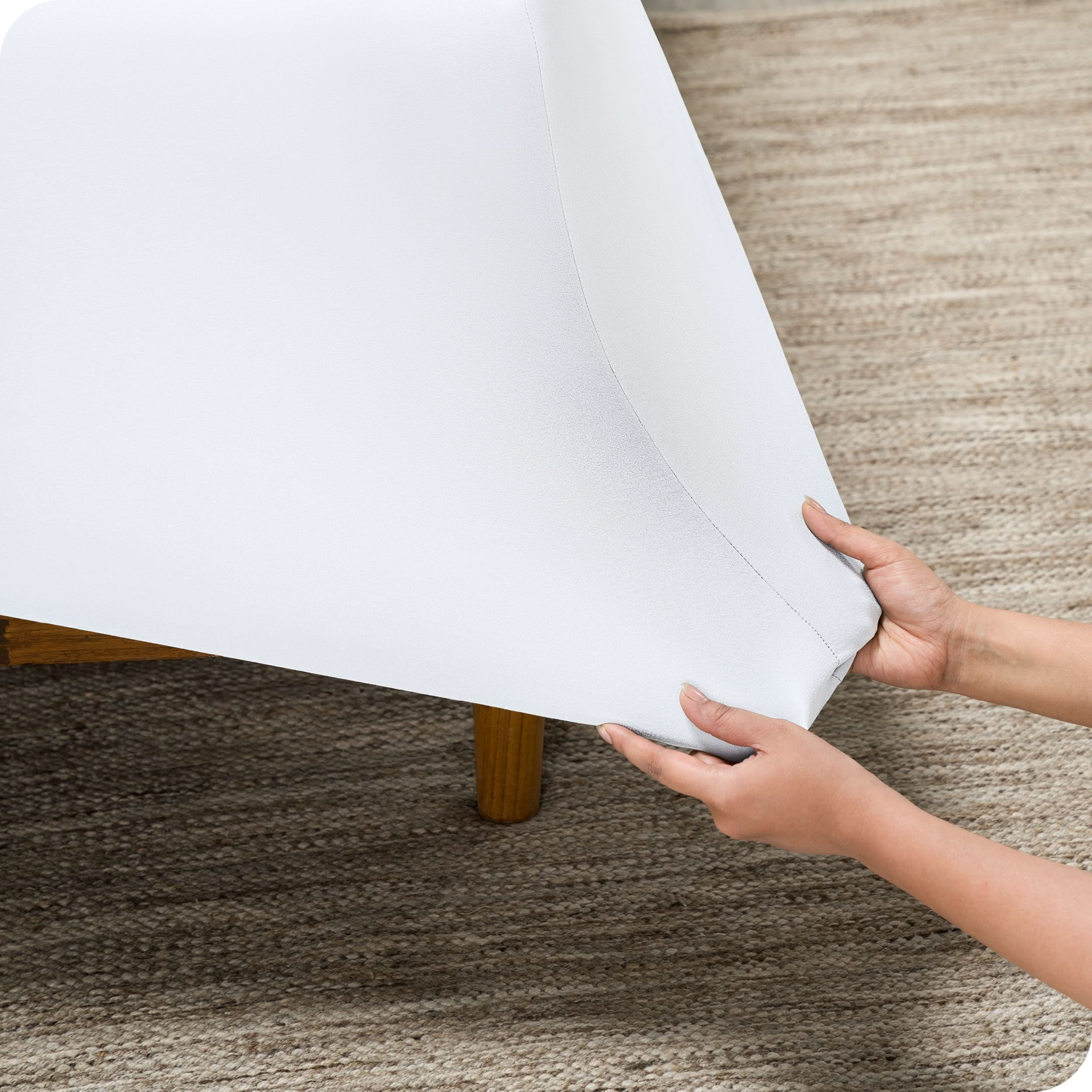 A person is pulling on the corner of a fitted sheet that is on a mattress