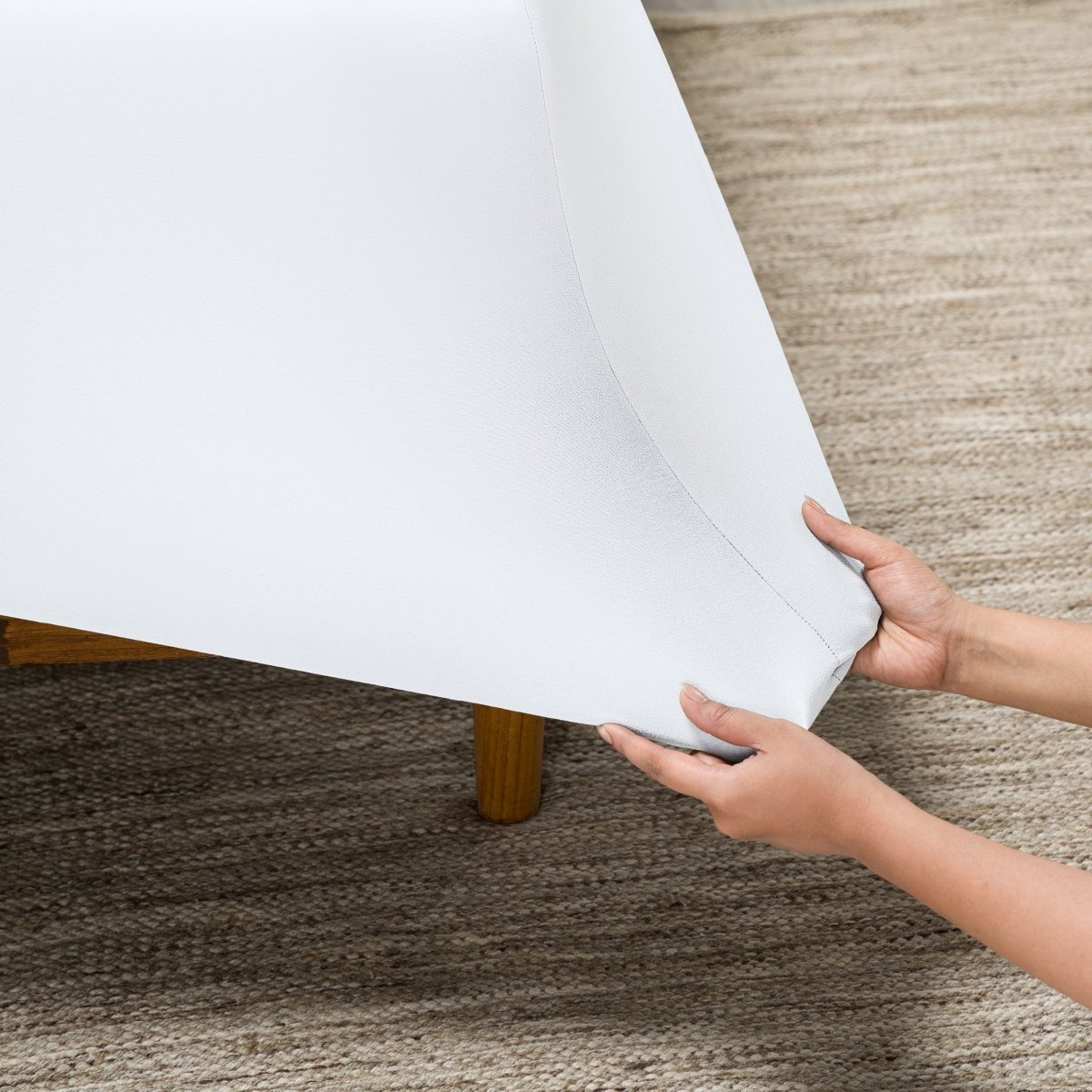 Person putting a fitted sheet on a bed on carpeted floor.