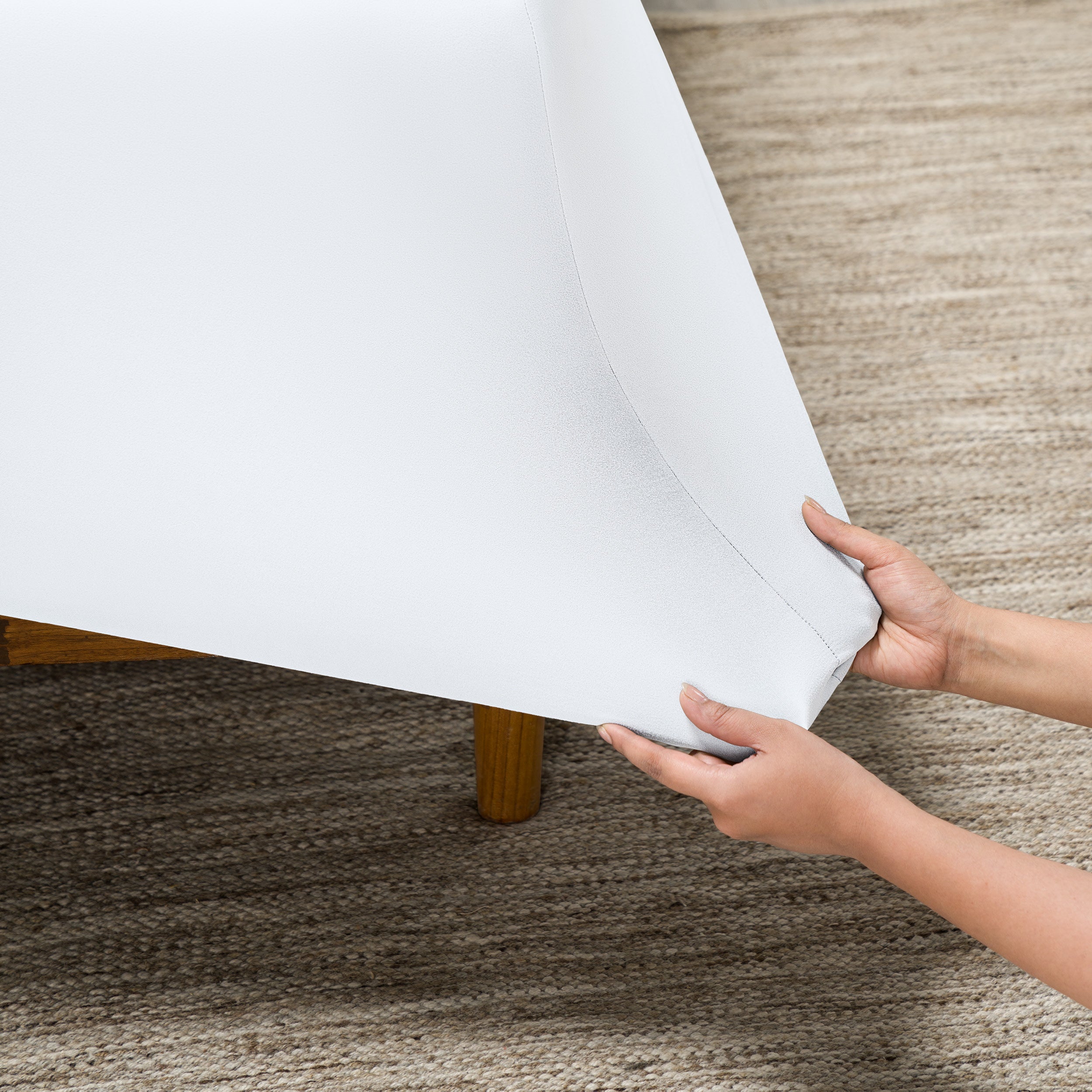 Person putting a fitted sheet on a bed on carpeted floor.