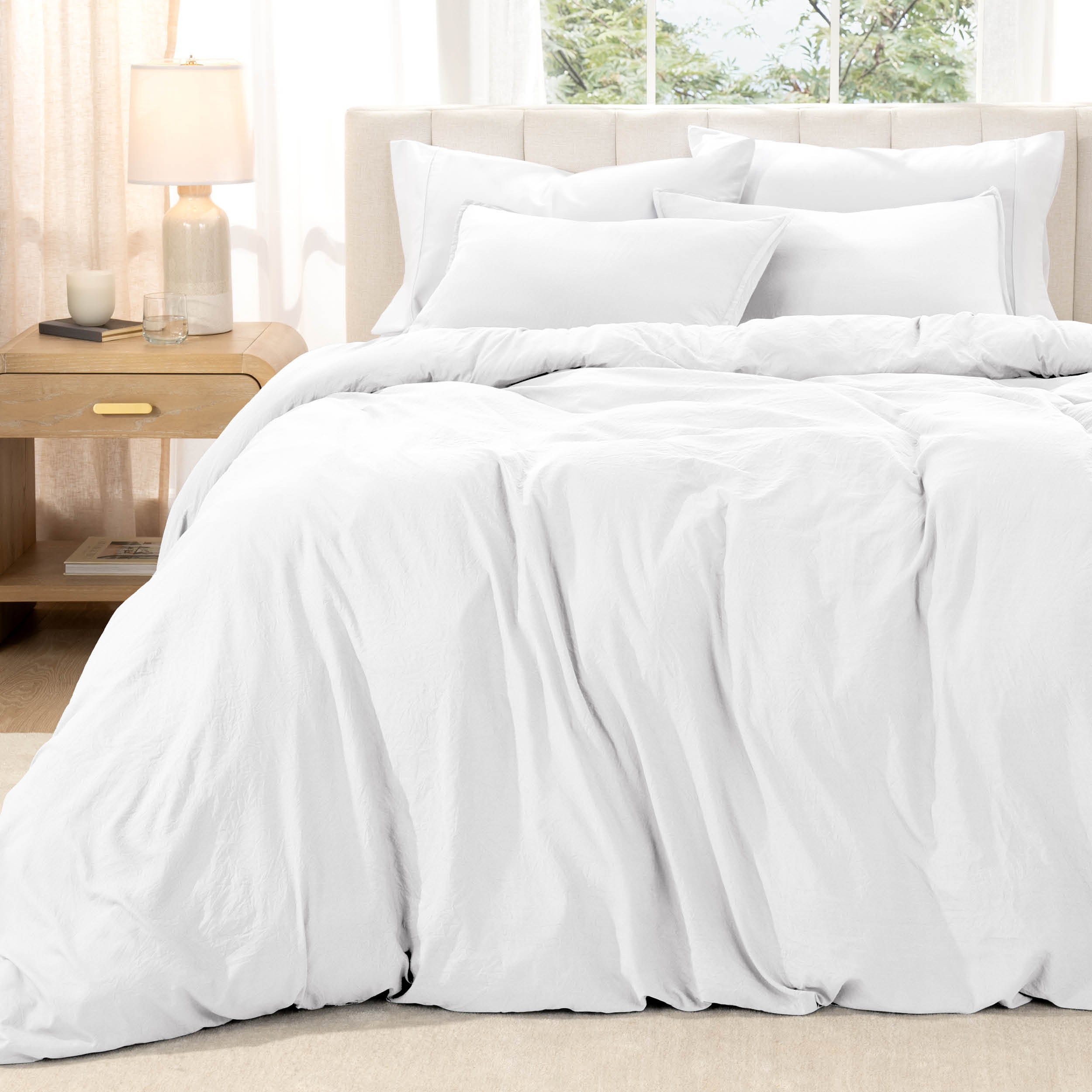Bed with washed bedding and white pillows in a bright room