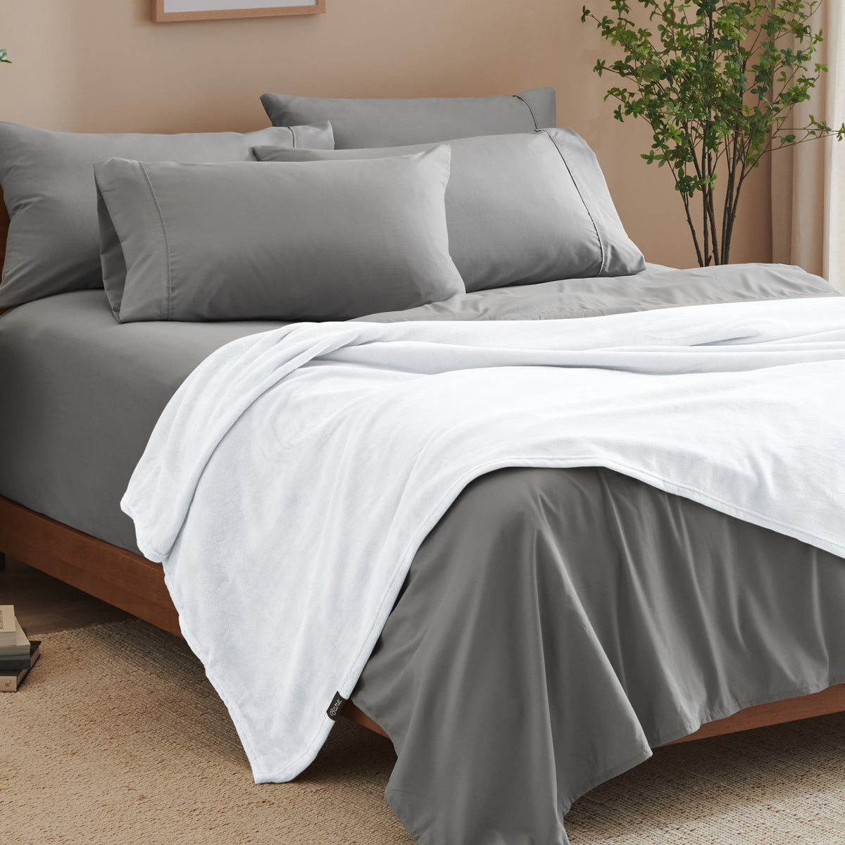 A bed made with grey sheets and a microplush blanket