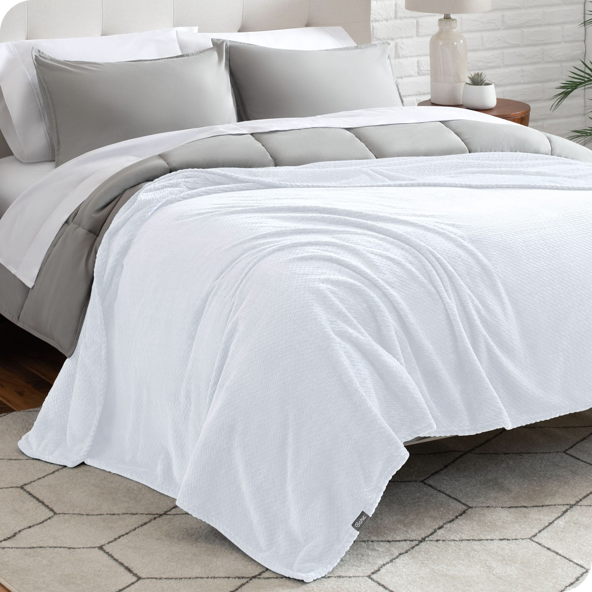 A textured microplush blanket is covering a bed, which has a comforter set on it.