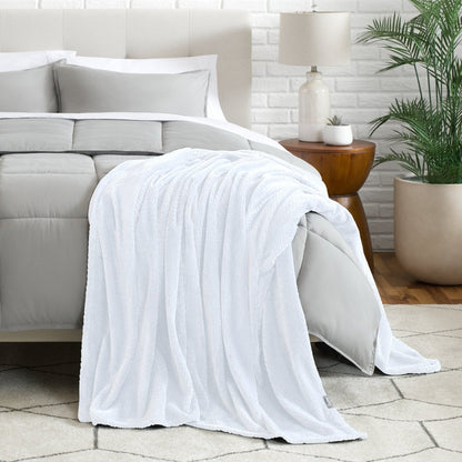 Blanket draped over a bed in a bedroom setting with a lamp and plant.