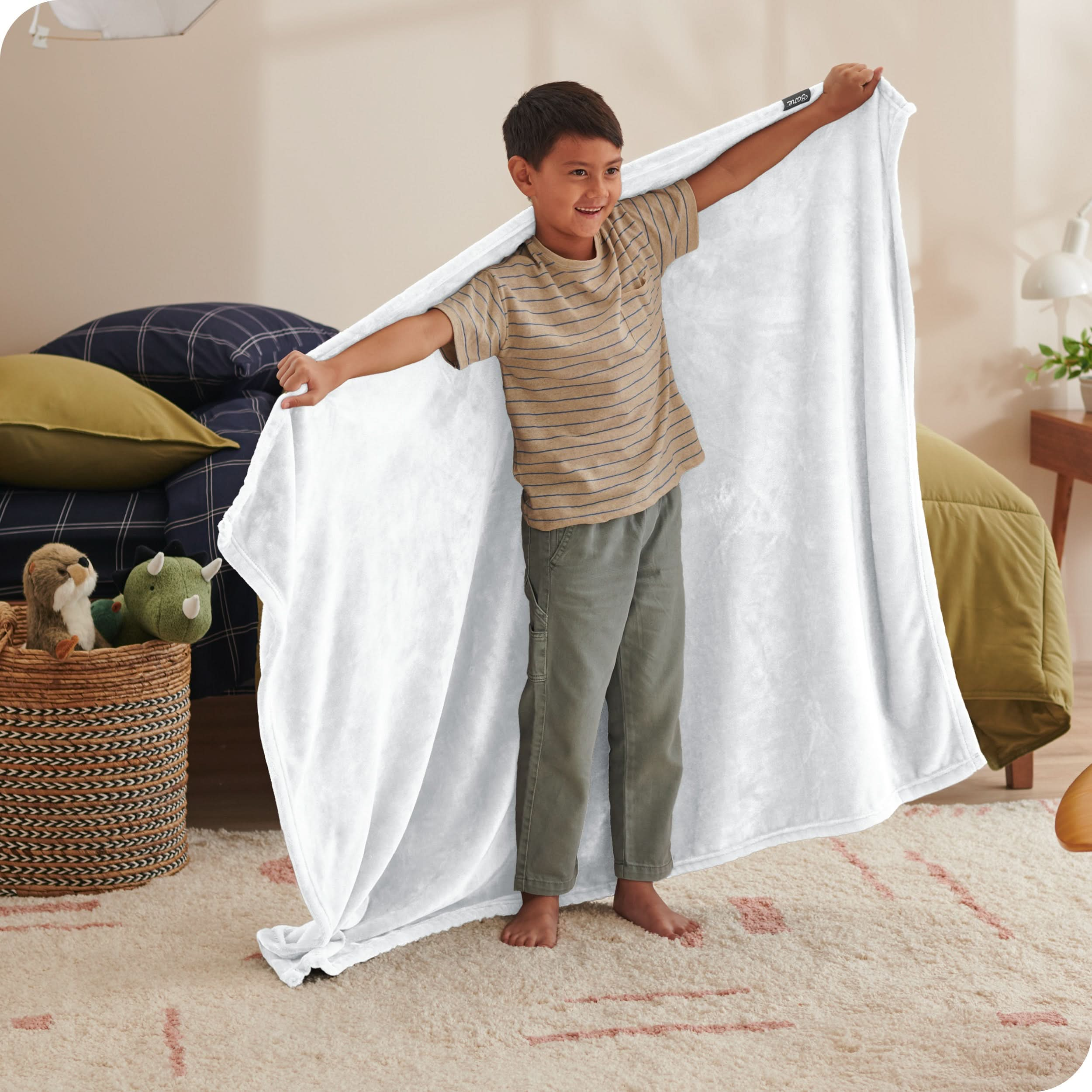 A child has his arms stretched out while holding a microplush blanket behind him