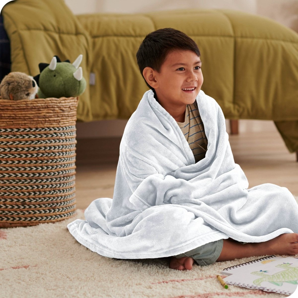 A boy is sitting on the floor of his bedroom with a microplush blanket wrapped around him