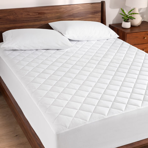 Quilted mattress pad on a bed with wooden headboard and nightstand.