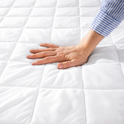 A woman is pressing her hand down on a quilted mattress pad