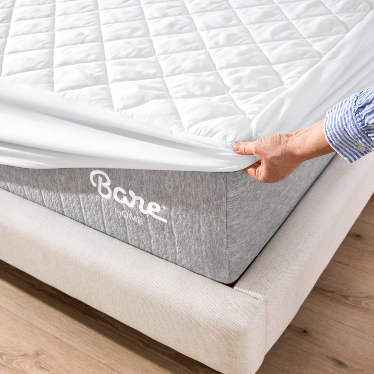 Person putting a mattress cover over a Bare Home branded mattress on a wooden floor.