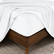 The corner of a bed frame and mattress with a fitted sheet and flat sheet on it.