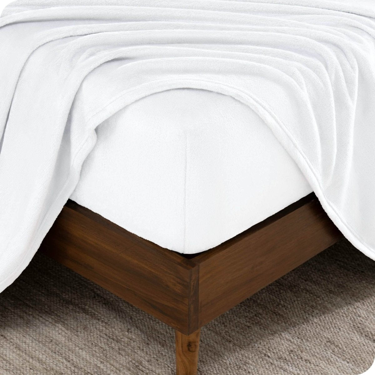 The corner of a bed frame and mattress with a fitted sheet and flat sheet on it.
