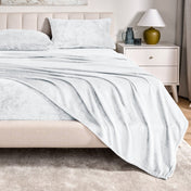 Microplush sheet set on a bed in a bedroom setting with a nightstand and lamp.
