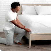 Man putting the corner of fitted sheet on a mattress