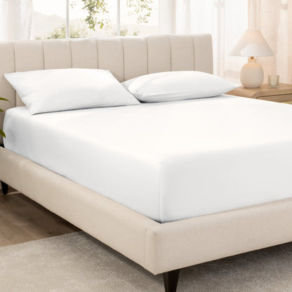 Bed with fitted sheet and pillowcases in a bright room.