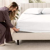 Woman adjusting a fitted sheet on a bed in a bedroom setting