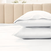Two pillows stacked on a bed with a beige headboard.