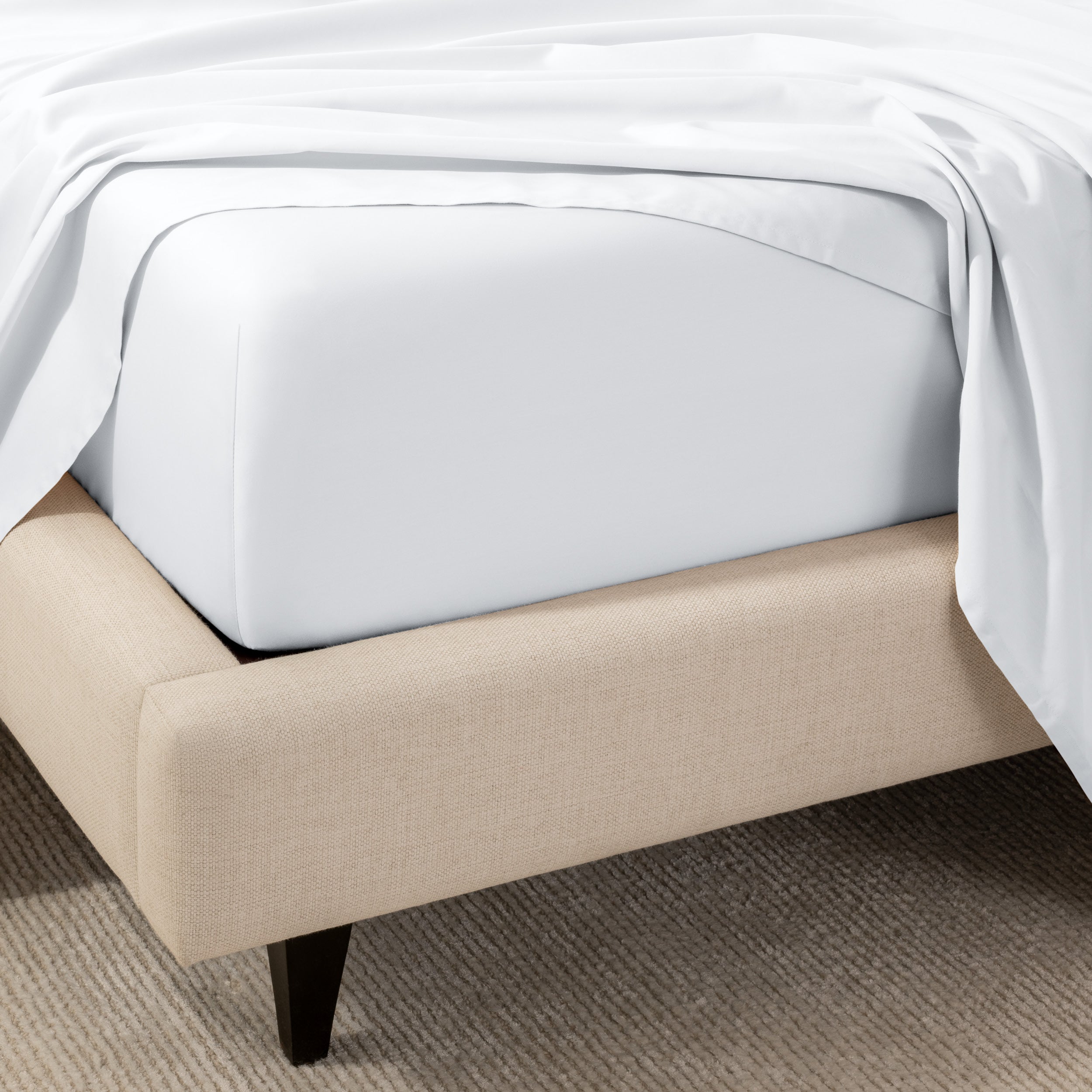 A close-up of the corner of a bed with a fitted sheet and matching flat sheet.