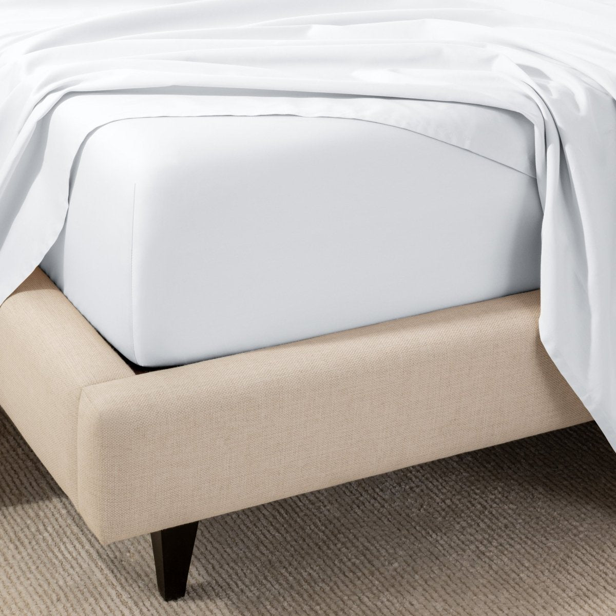 A close-up of the corner of a bed with a fitted sheet and matching flat sheet.