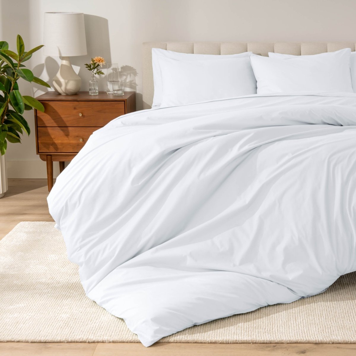 Percale bedding set on a bed in a bedroom with a wooden nightstand and lamp.