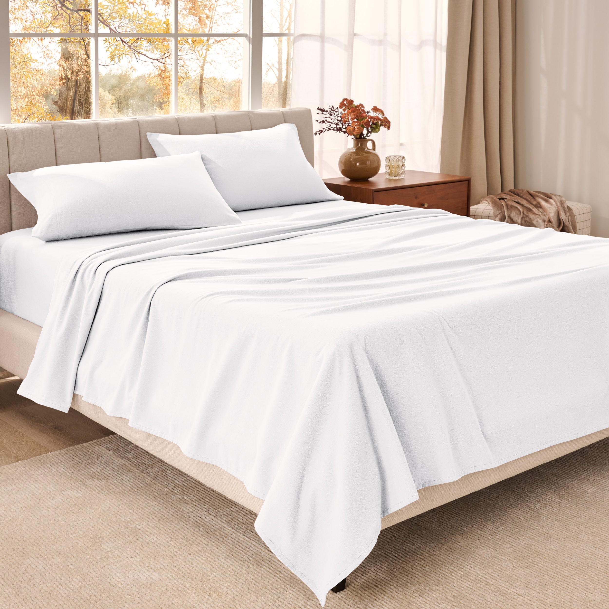 Bed sheets on a neatly made bed in a bright bedroom with large windows.