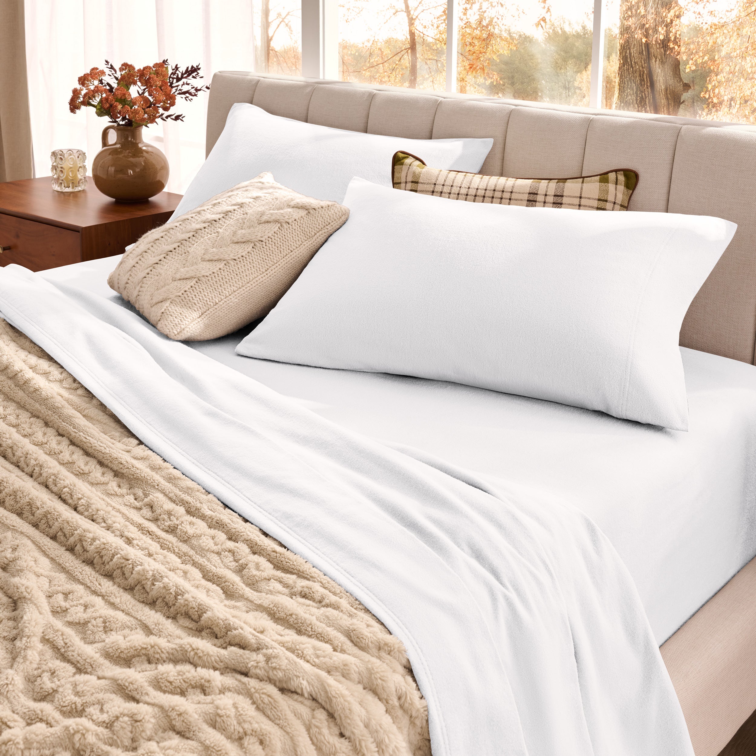 Neatly made bed with organic flannel sheets  and a beige blanket in a bright bedroom.