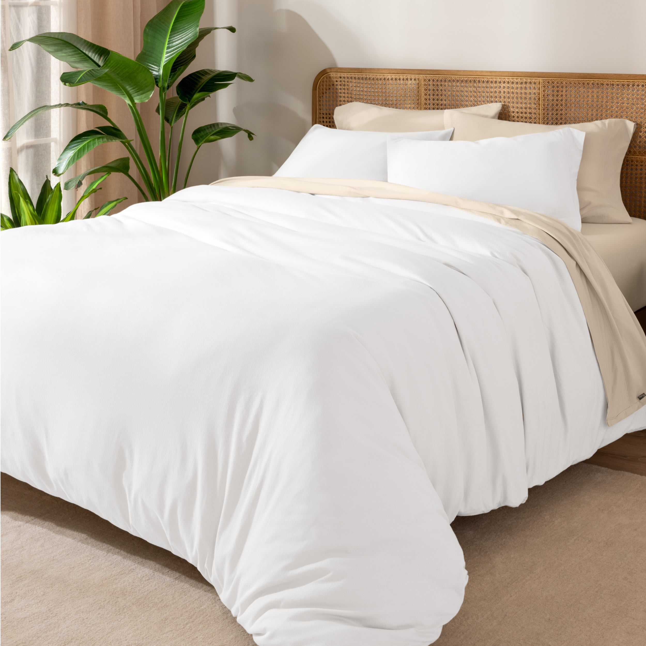 A cozy bed dressed in white sheets and pillows, complemented by an organic cotton jersey duvet cover set.