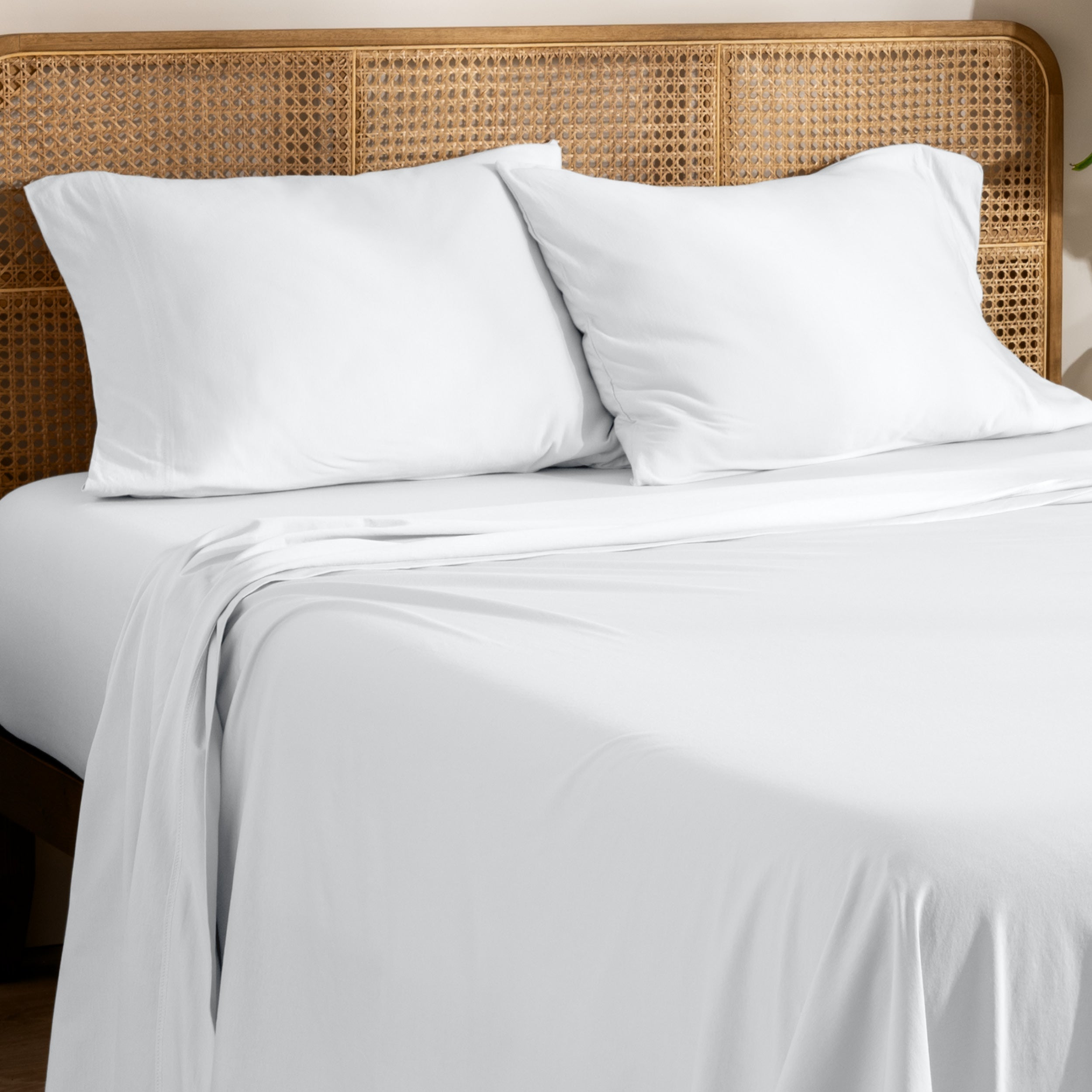 Organic jersey bed sheets and pillows on a bed with a wicker headboard.