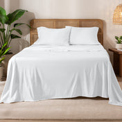 Organic cotton jersey sheets on a bed with a wicker headboard in a room with plants and a lamp.