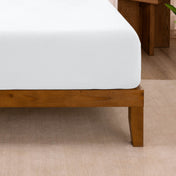 Fitted sheet on a wooden bed frame with a neutral background
