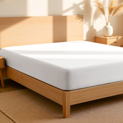 Fitted sheet on a bed in a bedroom setting with a lamp and plant.