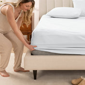 Woman in pajamas adjusting bed sheets on a bed.