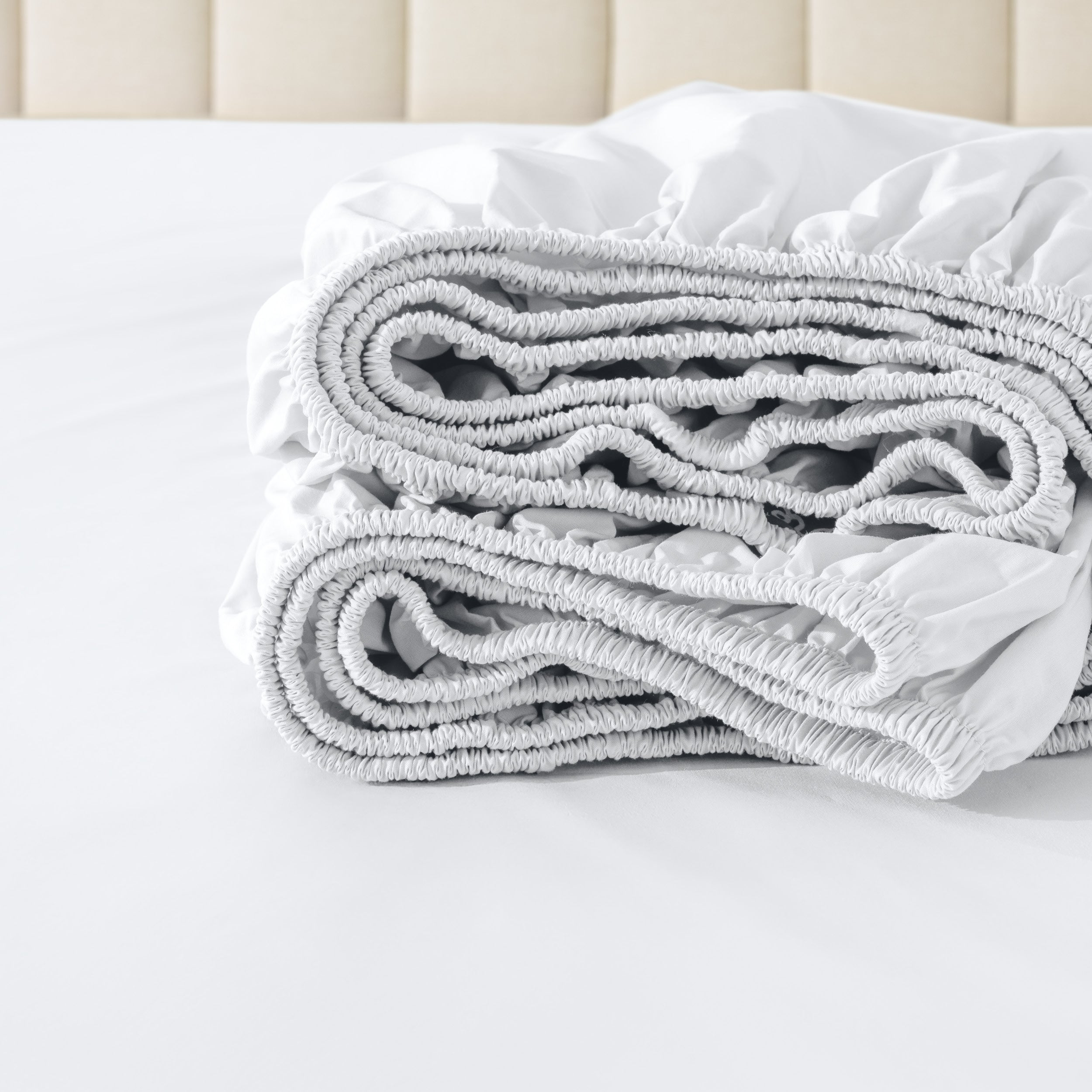 Folded fitted sheet on a bed with a neutral background