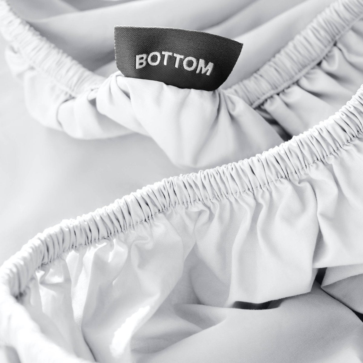 Close-up of a fitted sheet with a black fabric brand label reading BOTTOM.