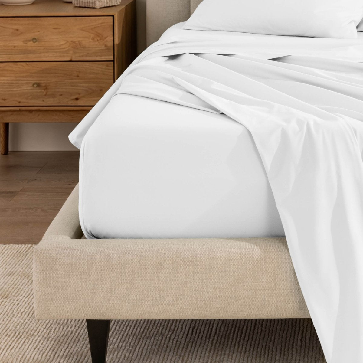 Top sheet and a matching fitted sheet on a bed with a beige bed frame