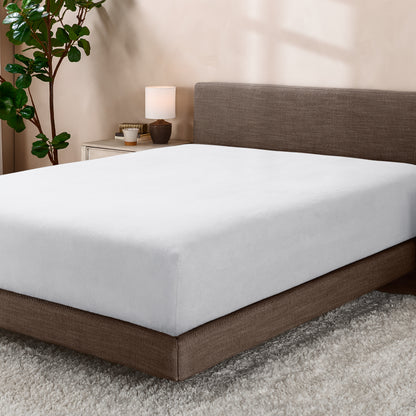 Bed with fitted sheet in a room with a lamp and plant.