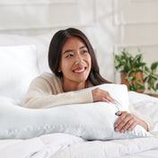 Woman lying on a bed with a body pillow, smiling.