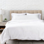 White satin pillow on a bed with white bedding and a wooden headboard.