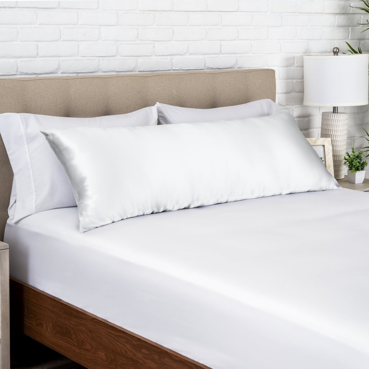 White satin pillow on a bed with white bedding and a wooden headboard.