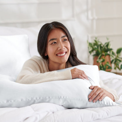 Woman lying on a bed with a body pillow, smiling.